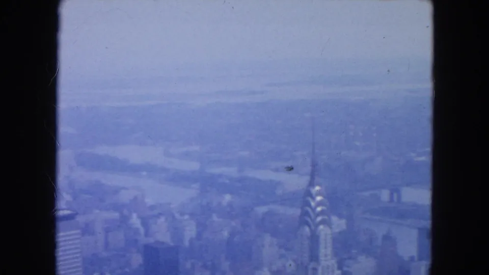 1954 New York City skyline view with the Chrysler Building, East River, and distant waterfront seen through grainy 8mm film.