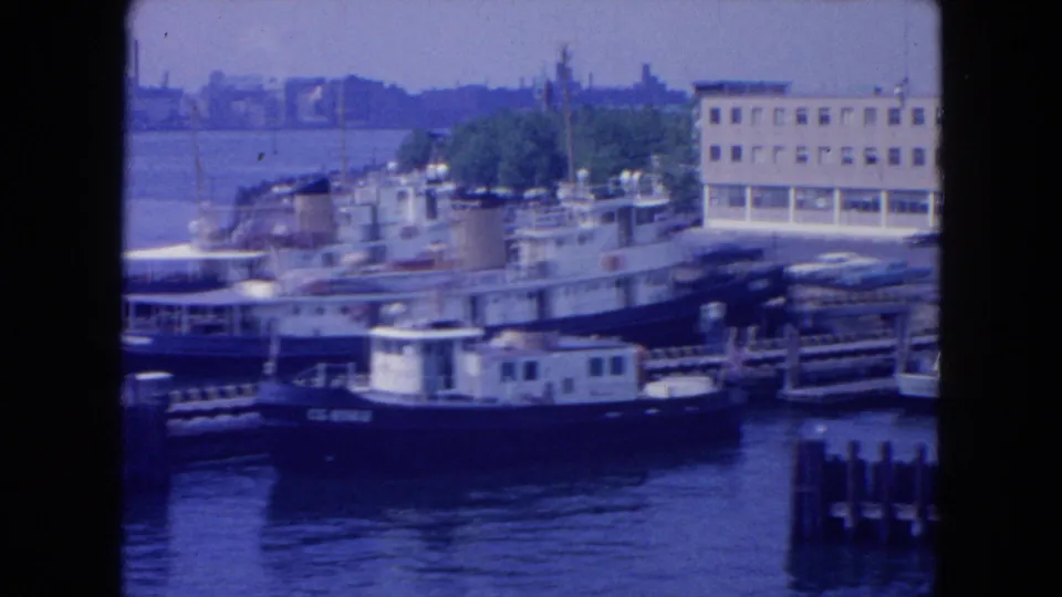 1954 New York City harbor frame showing tugboats and docked vessels along the East River waterfront in soft 8mm color.