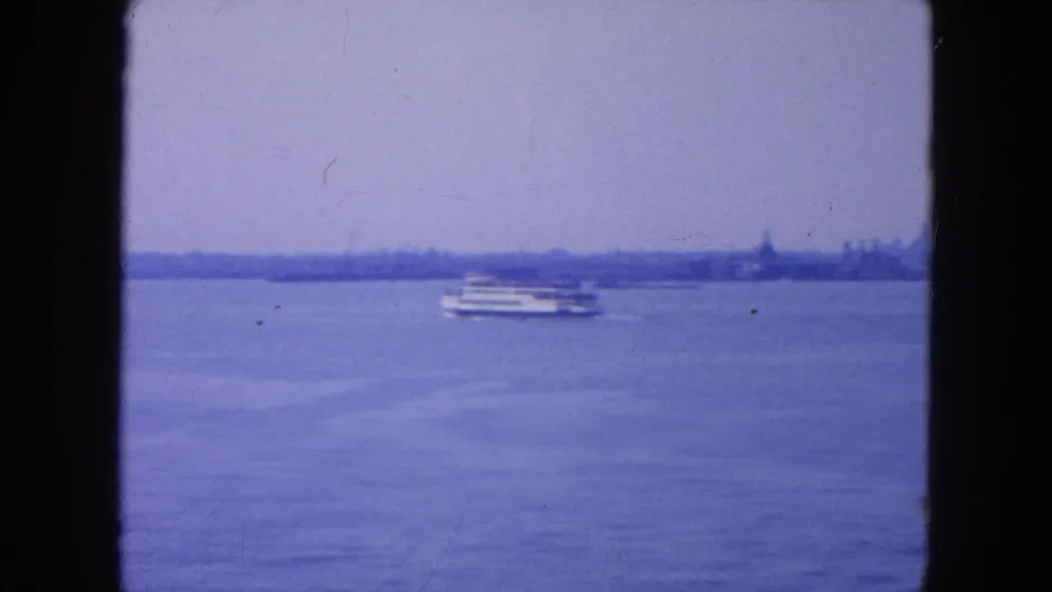 The ferry continues across open New York harbor, with a faint mid-century skyline stretching along the far shore.