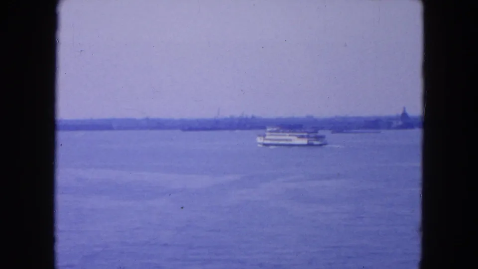 1954 8mm New York City harbor view with blue water, a distant passenger boat, and a hazy shoreline framed by film gate edges.