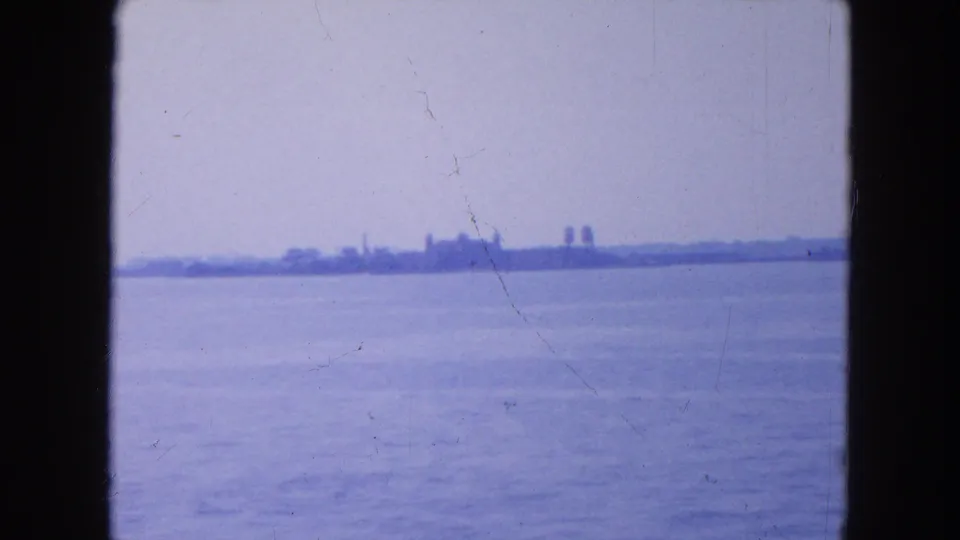 1954 New York City harbor view with open water, a distant shoreline, faint structures, and visible 8mm film wear.