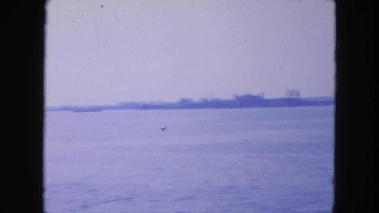 1954 8mm New York Harbor view from a boat, showing open water and a faint distant shoreline in blue haze.