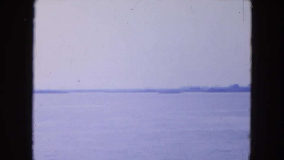 Soft 1954 New York Harbor view from the boat, with water, haze, and a low landform on the horizon.