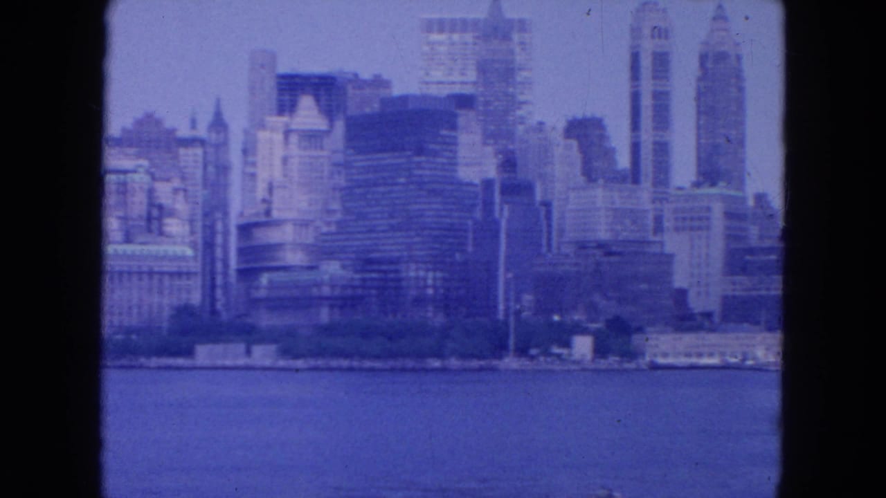 1954 8mm view of the New York City skyline across water, with tall mid-century buildings under a hazy blue sky.