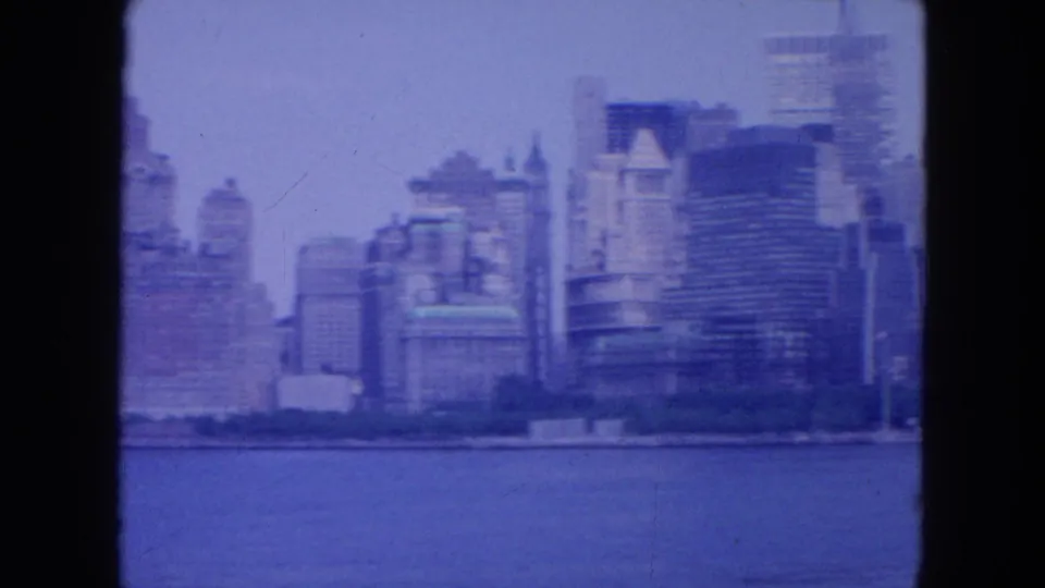The pan continues across New York City waterfront buildings and high-rises, softened by haze and 8mm film grain.