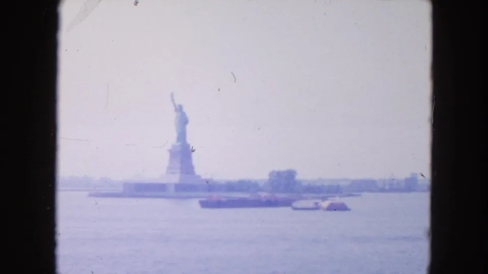 Distant 1954 New York Harbor view showing the Statue of Liberty, a barge, smaller boats, and faded 8mm color.