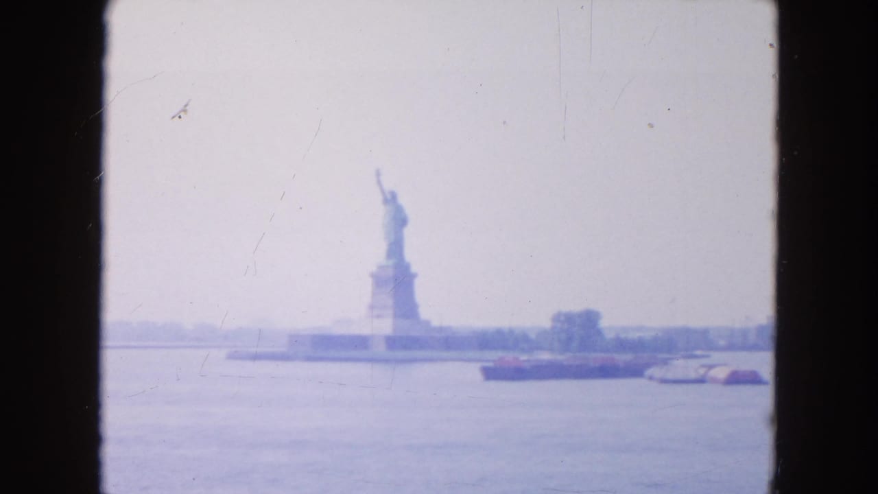 Distant Statue of Liberty across harbor water with a barge and dark frame borders.