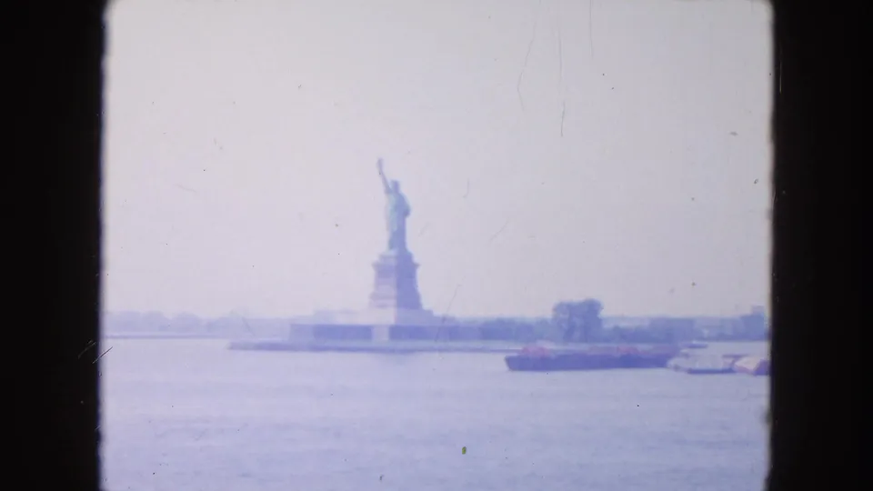Distant 1954 New York Harbor view of the Statue of Liberty, with a red barge crossing the water and softened 8mm color.