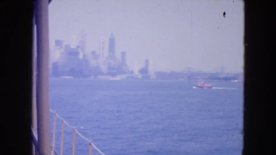 Distant New York City skyline across the harbor in 1954, seen from a vessel with railings at the left edge.