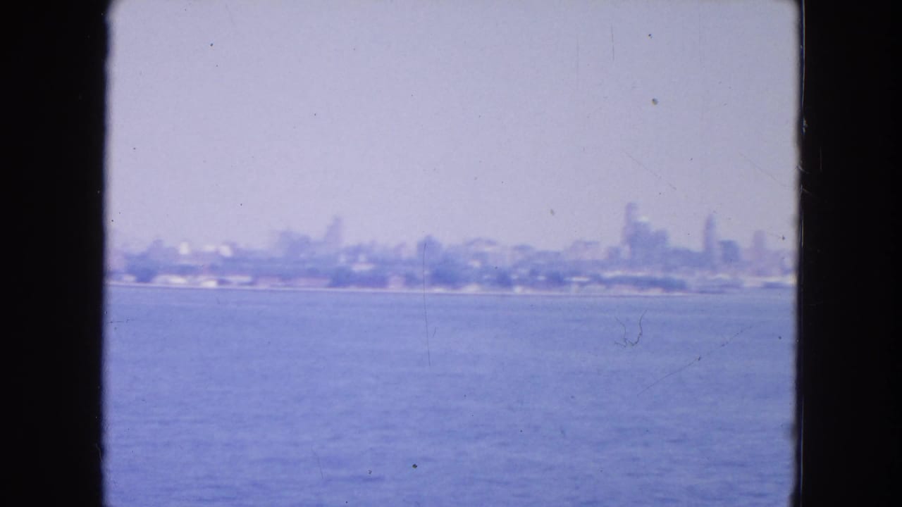 Distant hazy city skyline across water, framed by dark vertical window edges.