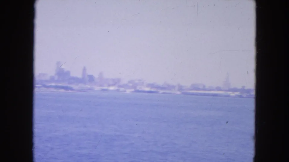 Distant New York skyline and low shoreline across harbor water, filmed through a dark-edged opening in 1954.