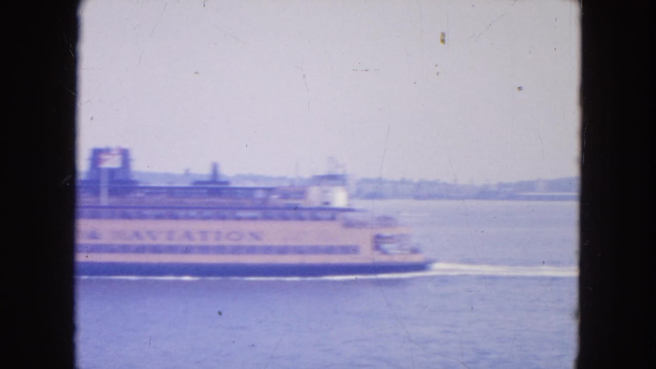 1950s New York harbor home-movie frame showing a Staten Island Ferry moving across hazy water with lettering on its side.