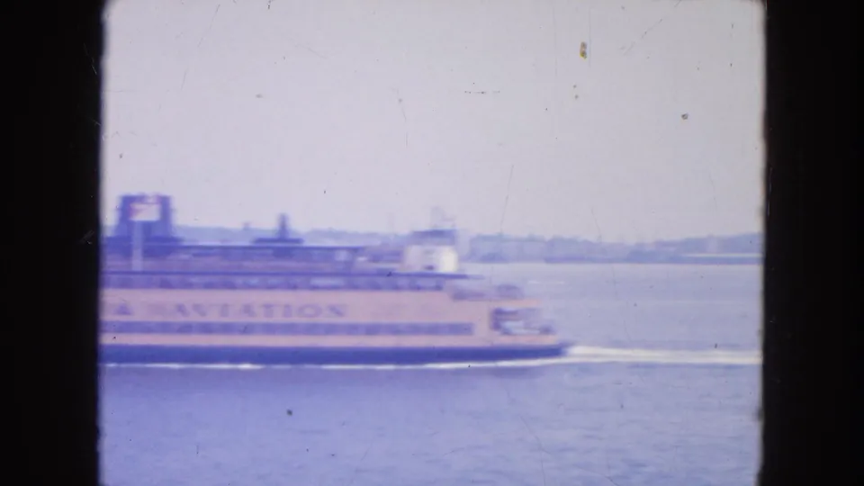 1950s New York harbor home-movie frame showing a Staten Island Ferry moving across hazy water with lettering on its side.
