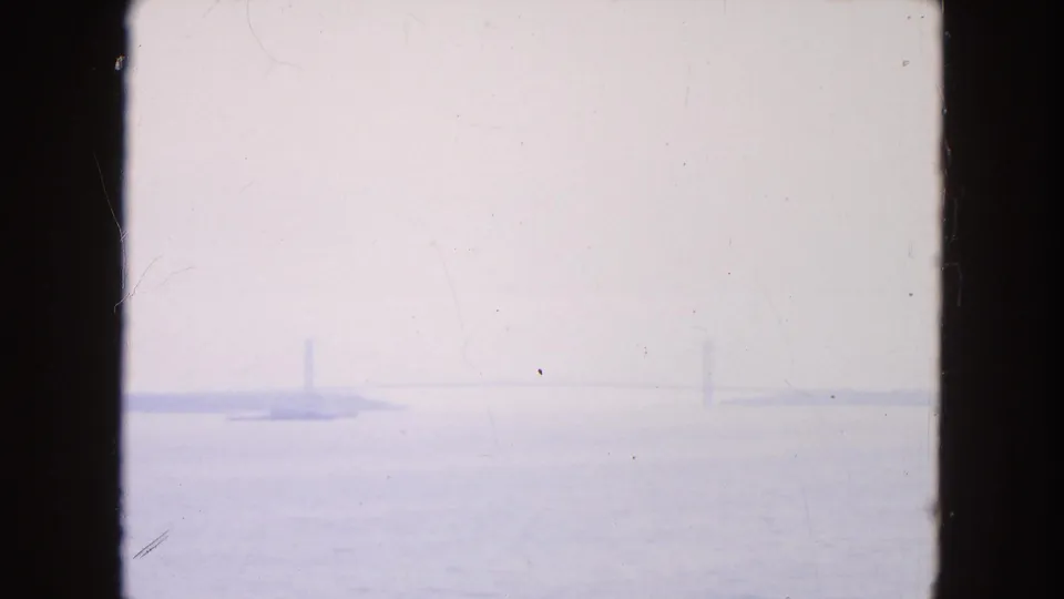 Final 1950s harbor frame showing open water, pale sky, and barely visible distant bridge-like forms through bluish haze.