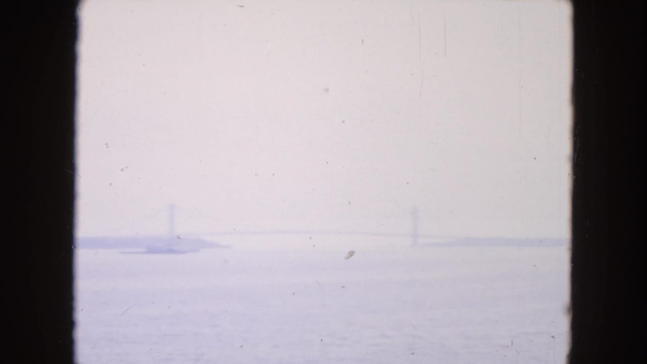 Hazy water view with distant barges and faint vertical structures beyond dark film borders.