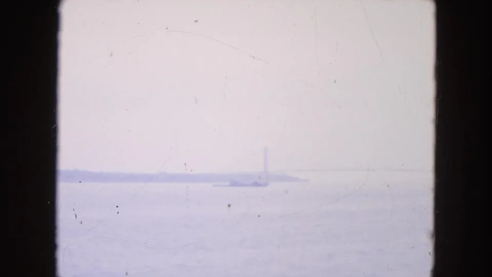 1954 New York City home-movie frame with a hazy river or harbor view, faint barges, and indistinct bridge or shoreline forms.