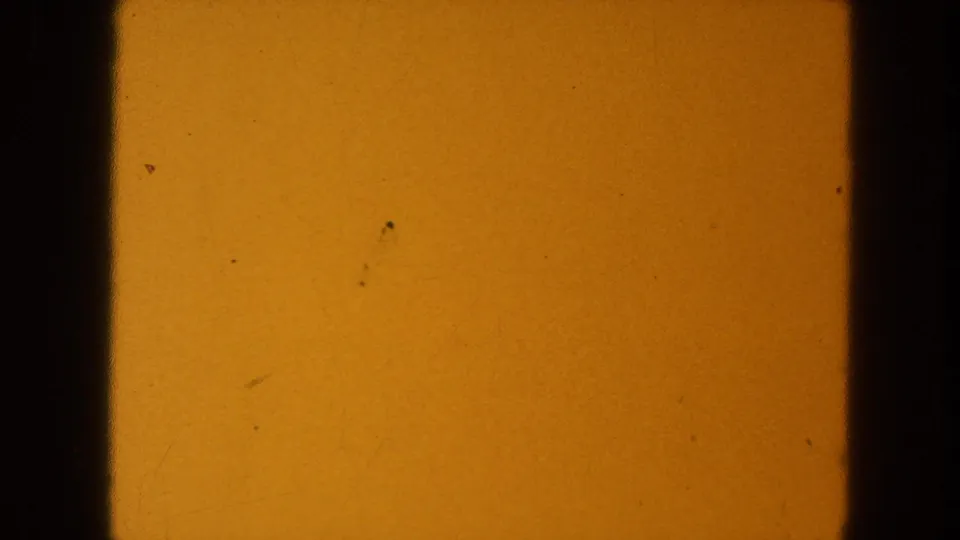 1954 8mm source frame showing yellow-orange exposure, black gate edges, scattered specks, and faint surface scratches.
