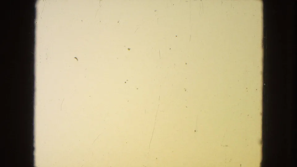 1954 8mm source frame with pale yellow exposure, dark vertical film edges, visible grain, dust, and fine scratch marks.