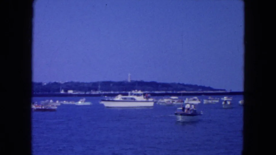 1954 New York City harbor footage showing yachts and small boats spread across blue water with a low shoreline beyond.