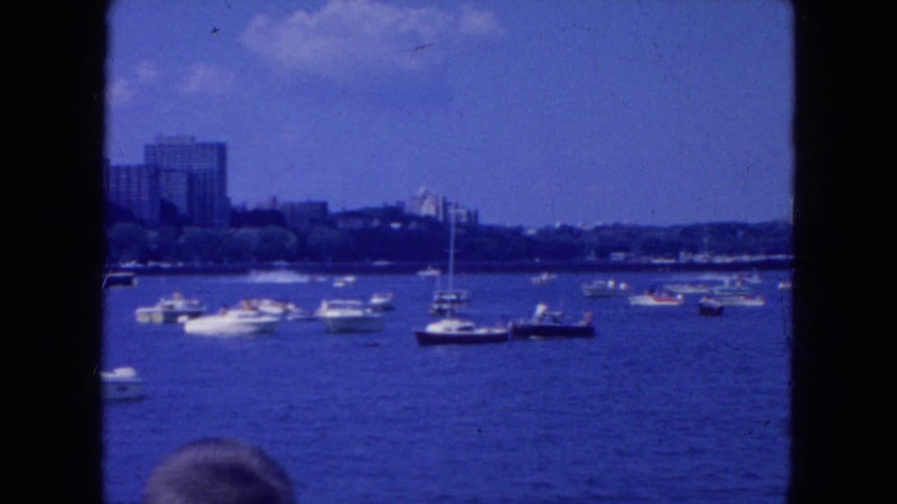Small boats on blue water with a distant city shoreline and dark frame borders.