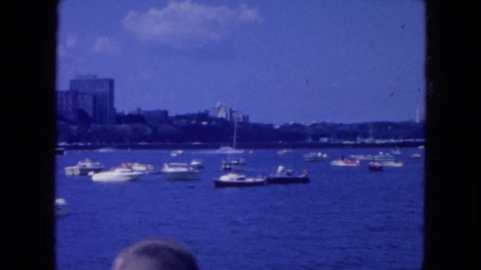 1954 New York City harbor view with multiple small boats, sailboats, distant buildings, and dark vertical frame edges.