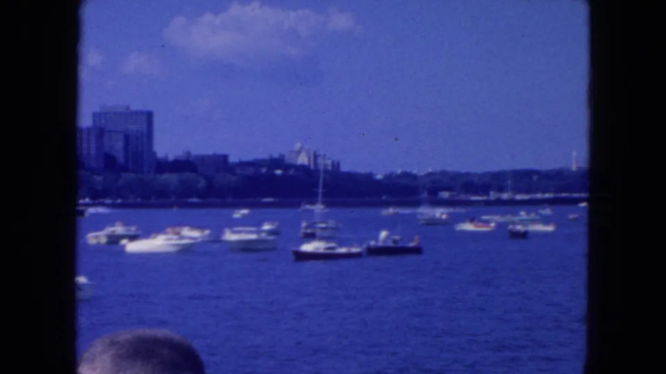 1954 New York City 8mm frame with sailboats and motorboats on a bright waterway, distant buildings, and a partial head in the foreground.