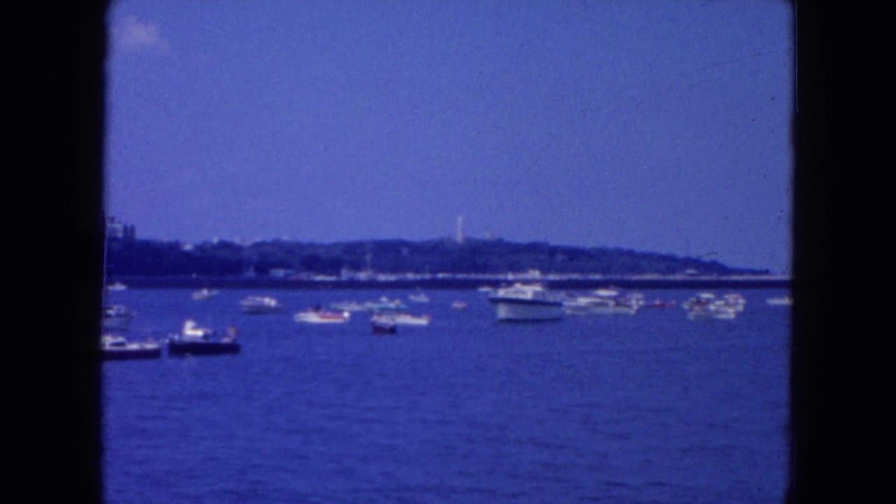 Waterfront view with small boats, distant shoreline, blue sky, and dark film-frame borders.