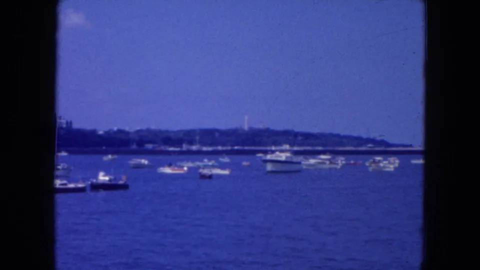 1954 New York City home-movie view across water with small boats and a distant shoreline under a blue sky.