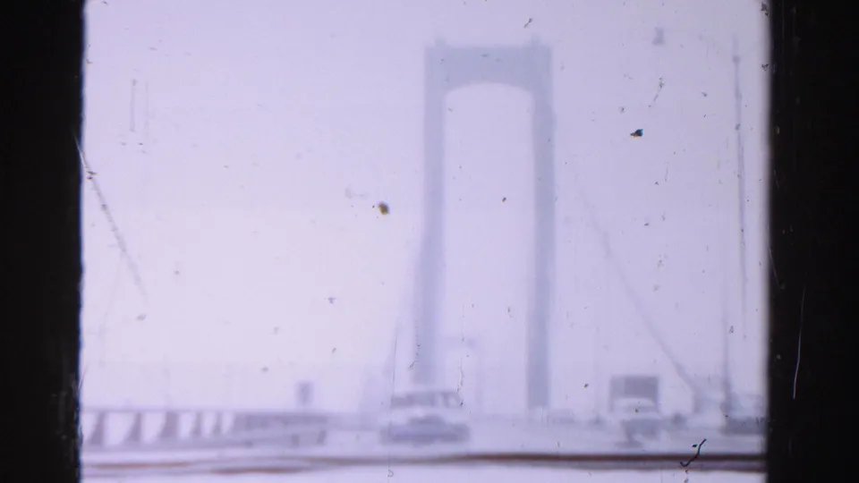 1955 Dade County footage shows a suspension bridge tower, roadway railing, and a small car in soft, hazy focus.