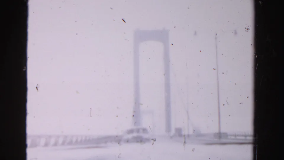 1955 Dade County frame with an approaching car on a suspension bridge roadway, seen through pale exposure and film dust.