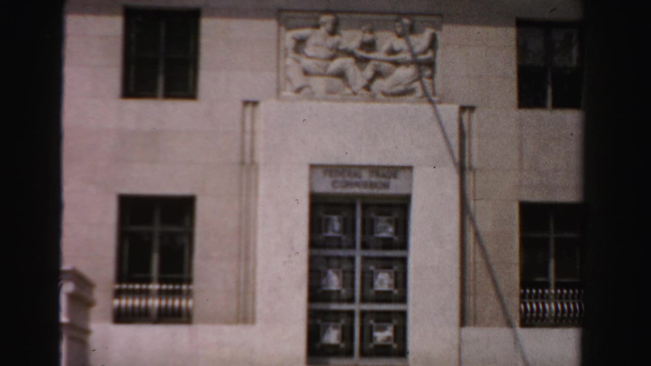 Pale civic building facade with sculptural frieze, windows, and multi-pane doors.