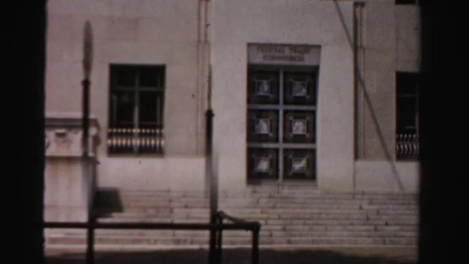 1950s 8mm frame of a building entrance from a moving vehicle, with steps, a streetlamp, windows, and relief detail.