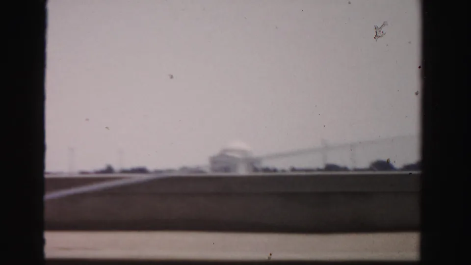 1950s 8mm frame looking through dark vertical framing toward water and a distant domed memorial-like building across the basin.