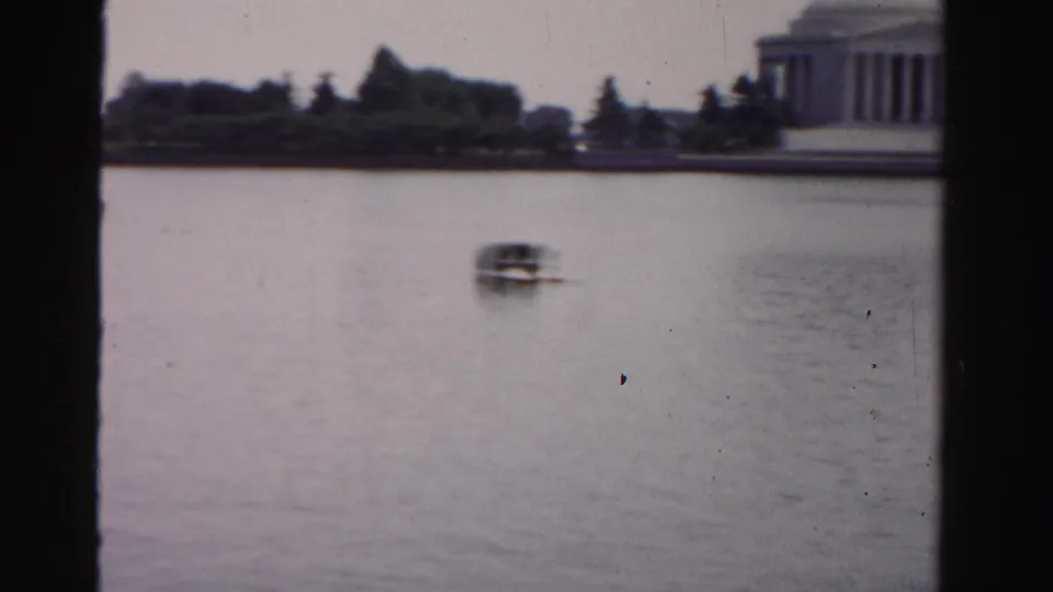 A small distant boat crosses open water, with trees and part of a columned memorial-like building visible along the far shoreline.