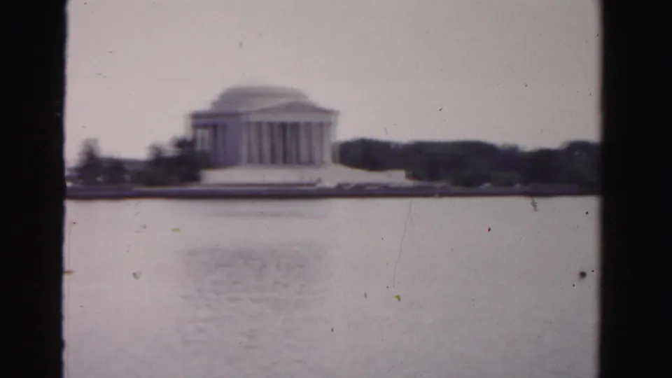 A domed, columned memorial-like building appears across the water, with trees along the shore in soft faded 8mm footage.