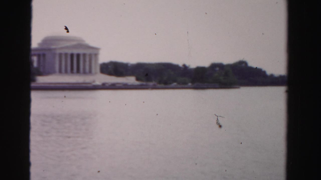 Distant memorial across calm water with trees and dark film borders.