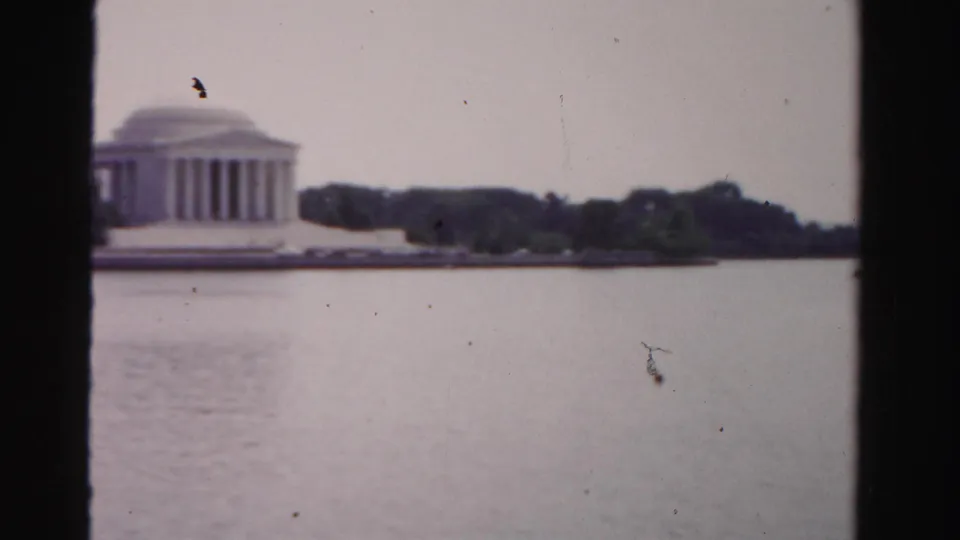Soft 1950s 8mm frame showing a distant Jefferson Memorial-like building across water with trees along the shoreline.