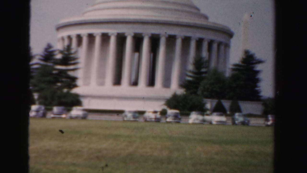 1955 8mm frame of the Jefferson Memorial in Washington, D.C., with parked mid-century cars, lawn, trees, and film edge framing.