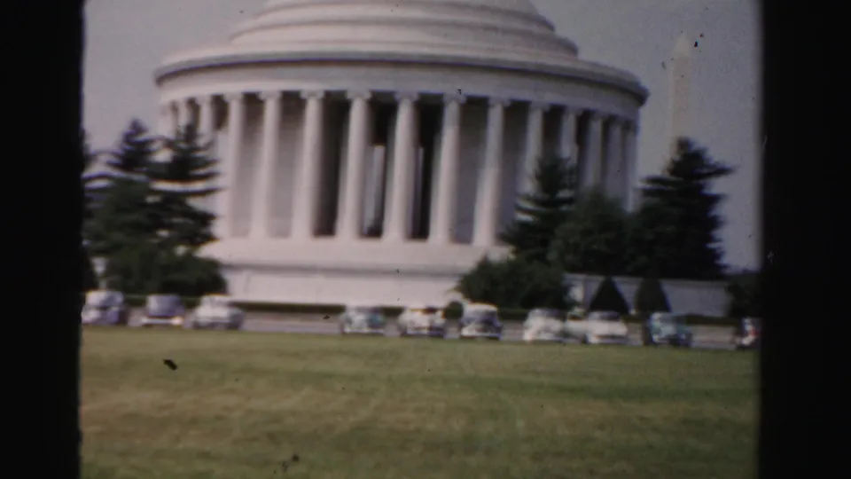 1955 8mm frame of the Jefferson Memorial in Washington, D.C., with parked mid-century cars, lawn, trees, and film edge framing.