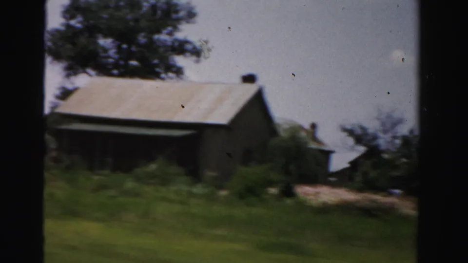 1955 Dade County roadside building with a pale roof, trees, grass, and yard space, softened by motion blur from the car.