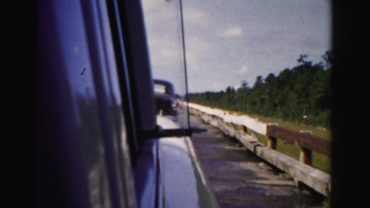 Passenger view in Dade County, Florida, showing the car door edge, side mirror, paved road, white guardrail, trees, and sky.