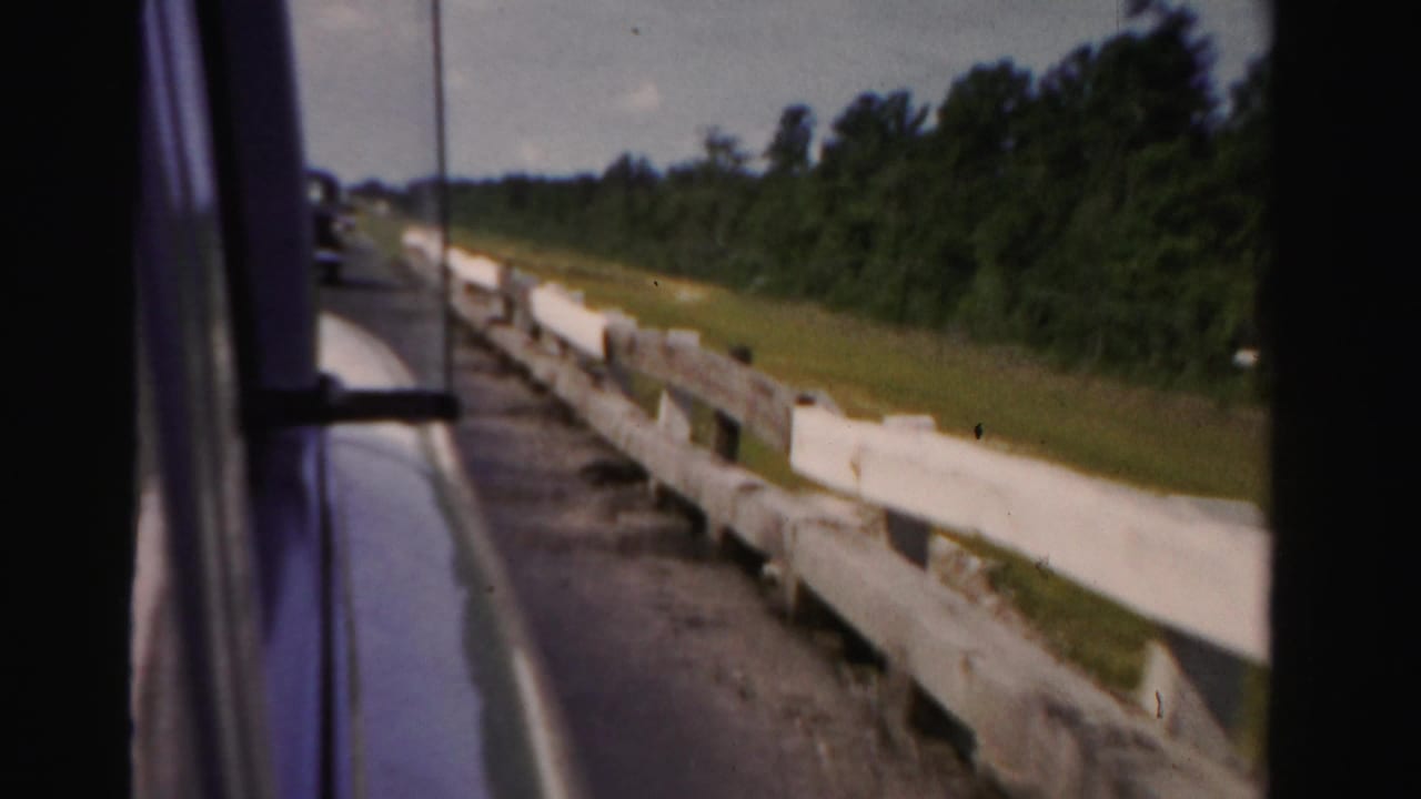 White roadside guardrail and trees seen beside a moving vehicle.