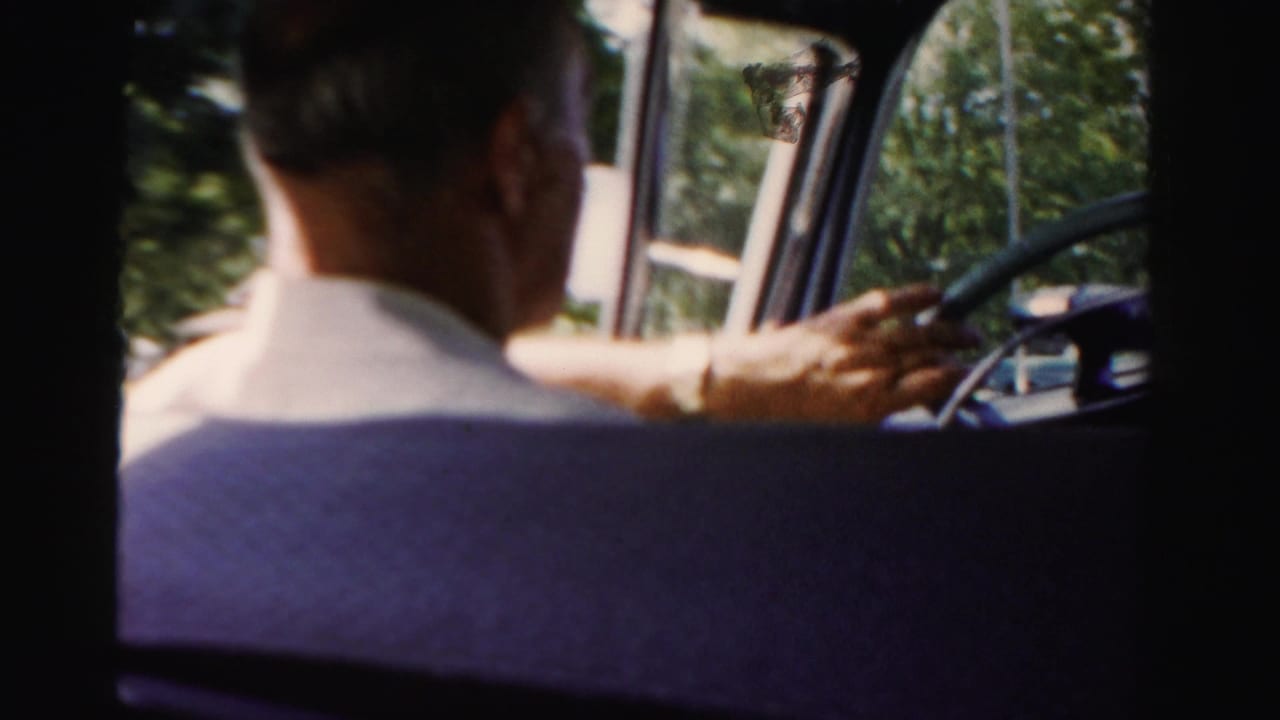 Driver seen from behind inside a car with hands near the steering wheel.