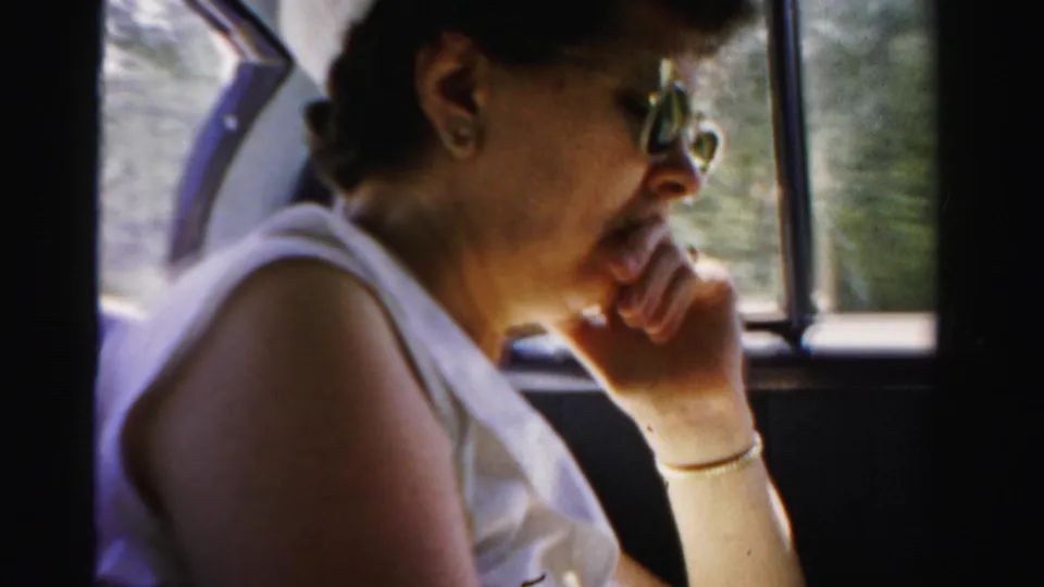 1955 Dade County home-movie frame showing an adult woman in profile, wearing sunglasses and seated inside a moving car.