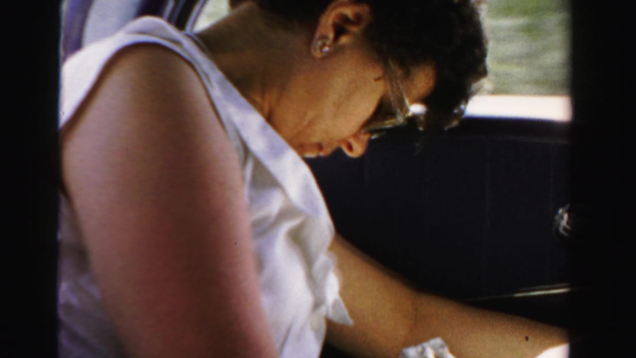 Woman in glasses sleeps inside a car, wearing a white sleeveless dress.