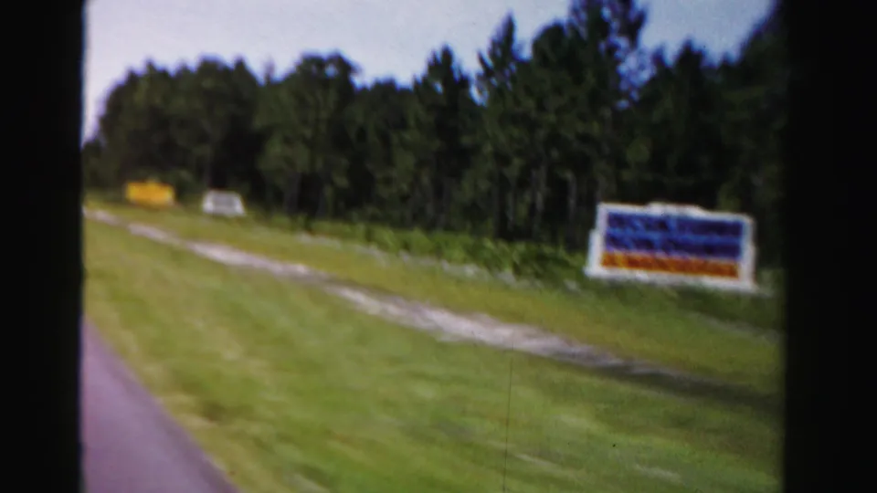 A 1955 Dade County road scene shows a grassy shoulder, dirt path, trees, and a passing roadside sign.