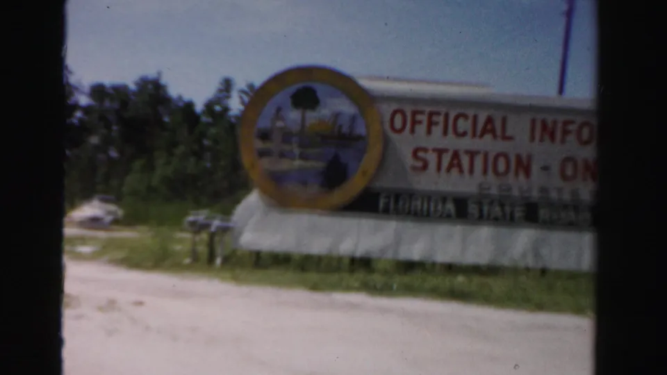 Large official information station sign along a Dade County roadside, filmed from a moving vehicle on 8mm film.