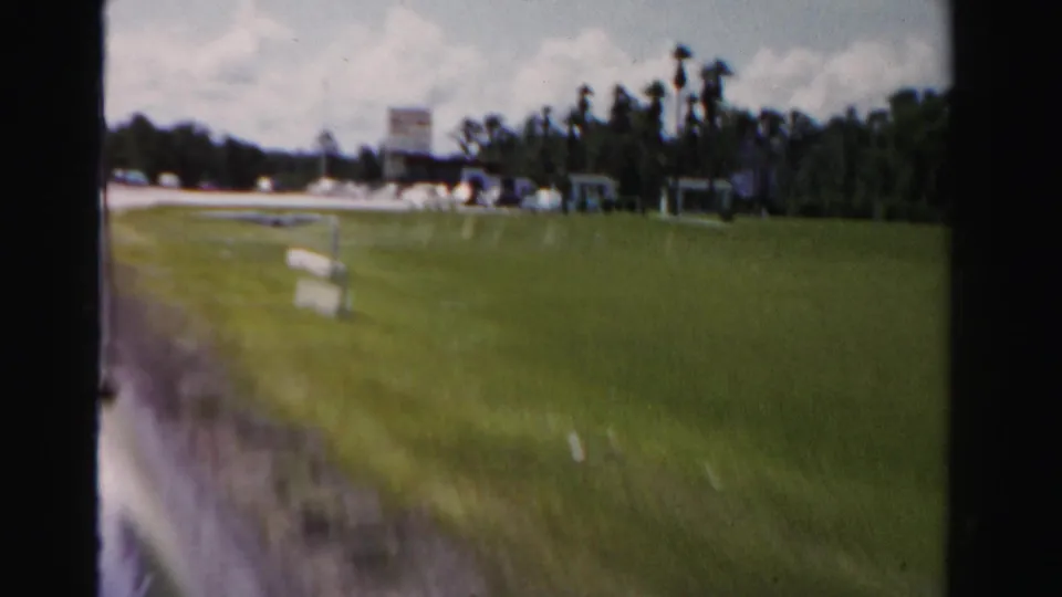 Dade County roadside scene with open grass, distant low buildings, scattered signs, trees, and the edge of the road.