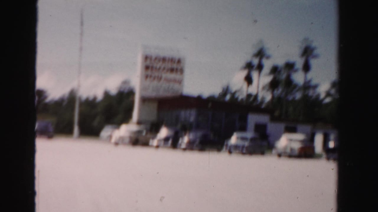 Florida welcome sign and parked cars in front of a low roadside building.