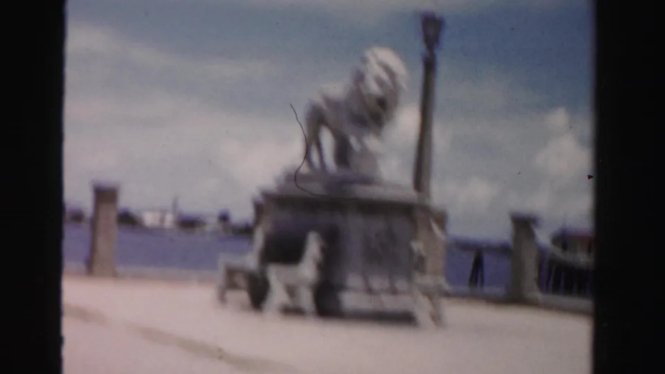 A brief Dade County travel view shows a lion statue on a pedestal by the water, with walkway features and a hazy shoreline beyond.